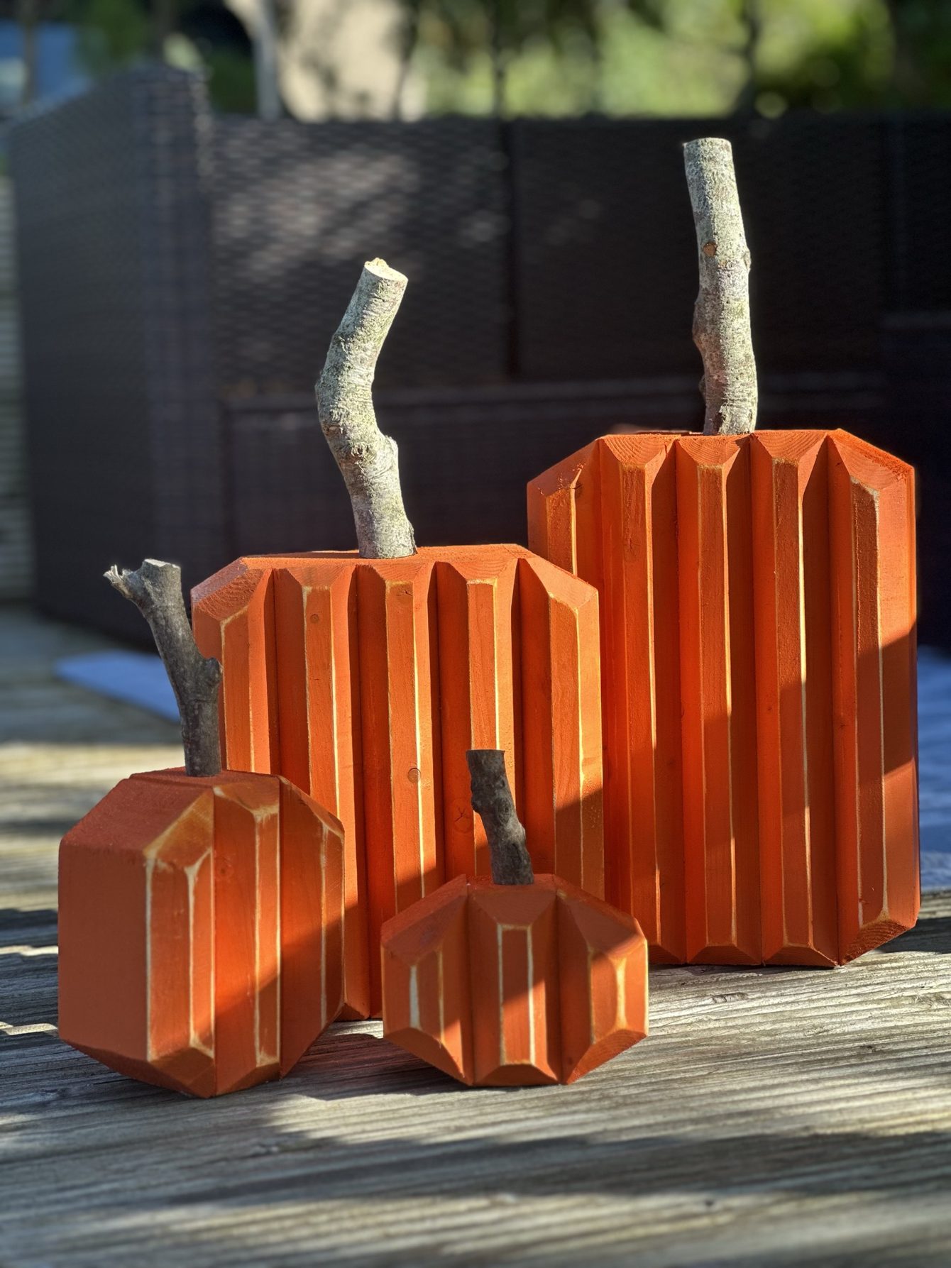 Three orange wooden pumpkins with branch stems on a garden deck.